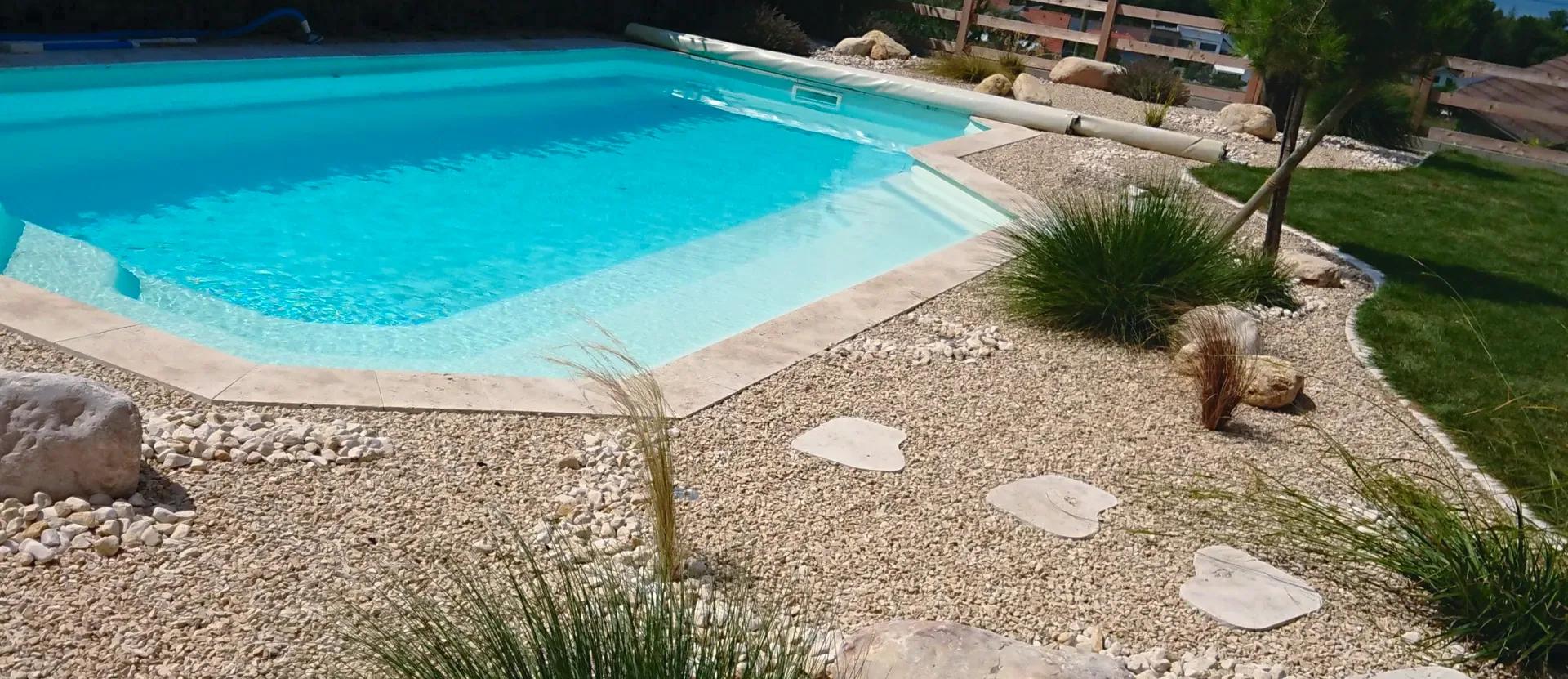 Abords de piscine aménagés en gravier clair, avec pas japonais, rochers et touffes de graminées